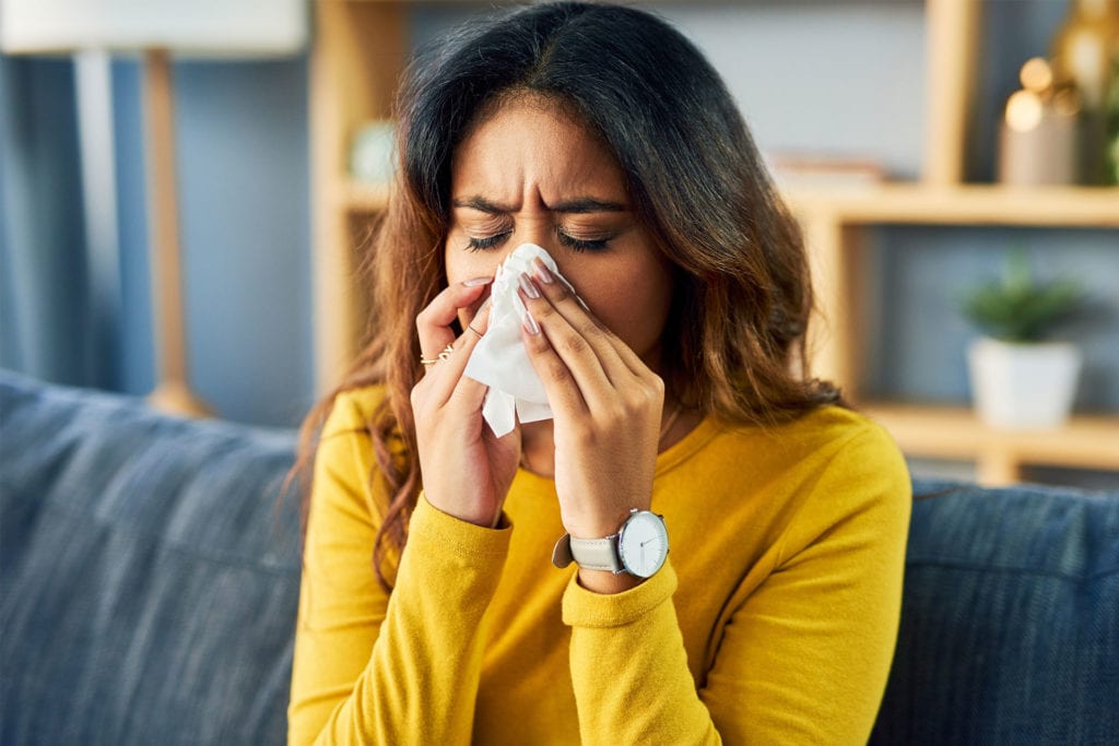 A woman with seasonal allergies blows her nose with a tissue. 