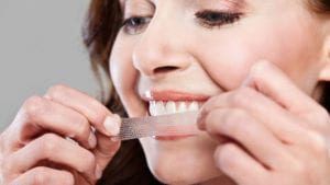 A woman whitens her teeth at home with whitening strips.